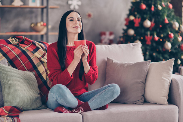 Photo of young cute lady sit couch hold cup eyes closed sniff smell wear red sweater jeans socks in decorated living room home indoors - Foto, Imagen