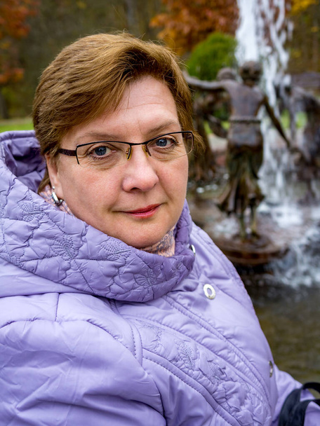 Reife, mollige Frau in Brille und blauer Jacke ruht in einem Stadtpark - Foto, Bild