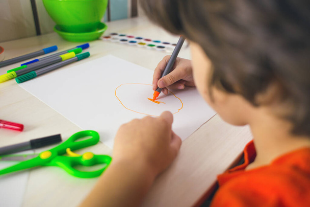 Le garçon dessine avec des stylos feutre sur papier, l'enfant est engagé dans la créativité, l'enfant fait ses devoirs. - Photo, image