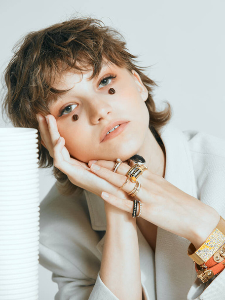 Pretty young female face with coffee beans. Dreaming girl with stylish short haircut, rings and bracelets on hand - Foto, imagen