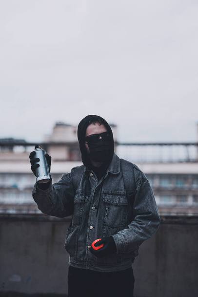 Anónimo en máscara y gafas comprueba lata de pintura en aerosol en el techo - Foto, imagen