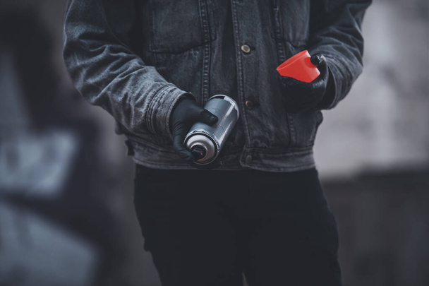 Man in denim jacket uses red fluorescent spray paint. Process making graffiti. - Foto, afbeelding