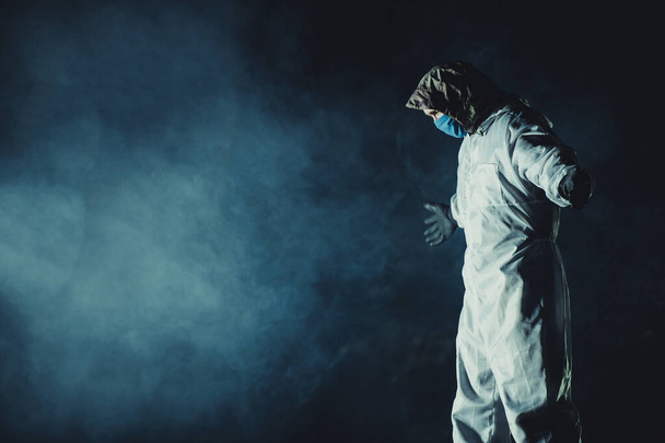Caucasian Men Wearing Blue Mask and Hazmat Suit in Dark Smoky Place with Stretched Hands. Conceptual Photo. - Foto, afbeelding