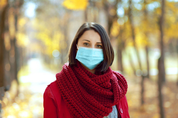Mooie jonge vrouw met medisch beschermend gezichtsmasker die in het najaarspark buiten loopt. Coronavirus sociale afstand concept. - Foto, afbeelding
