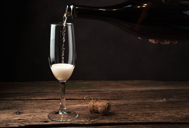 The champagne glass is just beginning to fill with alcohol with foam and bubbles on a wooden background. - Zdjęcie, obraz