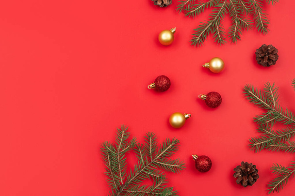 Christmas composition. Christmas background concept. Top view of Christmas red and golden balls with spruce branches and fir cone on red background. - Foto, Bild