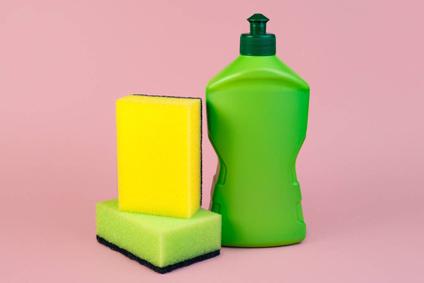Green bottle of dishwashing detergent and sponges on pink background. - Photo, Image