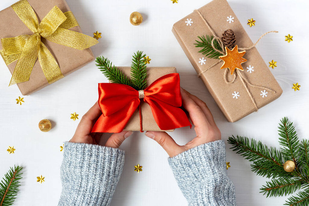 Woman's hands in woolen sweater hold a gift wrapped in vintage style next to two presents in eco-paper - 写真・画像