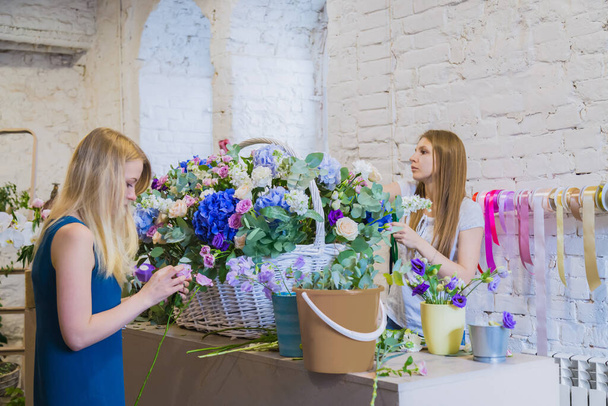 Δύο γυναίκες ανθοπωλεία κάνει μεγάλο καλάθι με λουλούδια σε φωτεινό δωμάτιο - Φωτογραφία, εικόνα