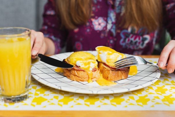 暑い夏の日にテラスのカフェで朝食をとる女の子。ベーコンと新鮮なオレンジジュースとポーチドエッグトースト。明るいライフスタイルの概念。友達とのランチタイム - 写真・画像