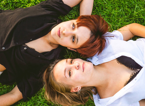 Girls couple in love lying on the grass in a park on a sunny day.  - Foto, afbeelding