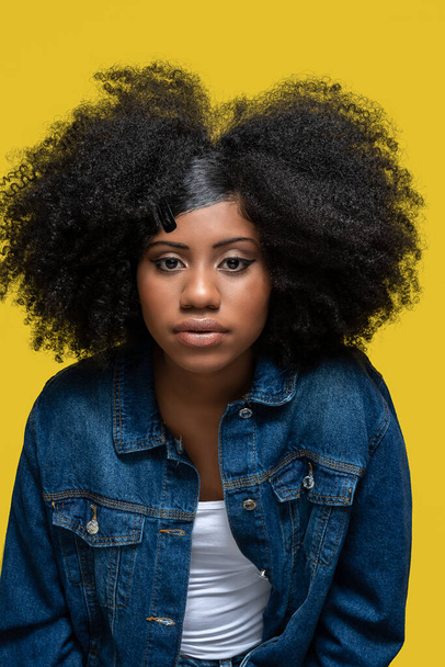 portrait of afro brazilian model wearing blue jeans jacket looking at camera isolated on yellow background - Foto, immagini