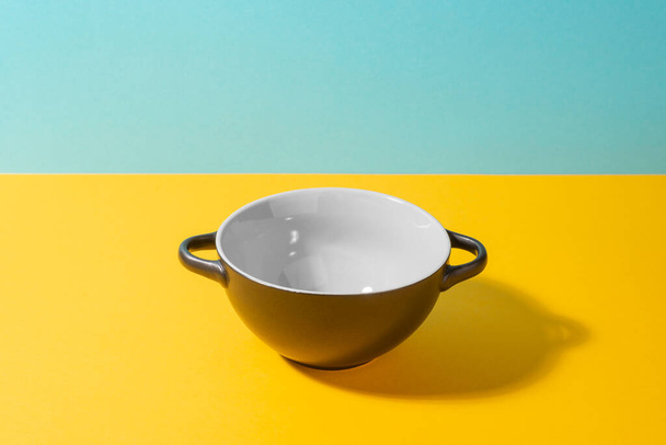 Black ceramic bowl on yellow and blue background - Фото, изображение