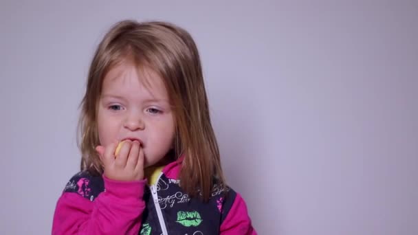 A csinos szőke lány szürkés hátterű sütit eszik. Teljes HD felvétel. - Felvétel, videó