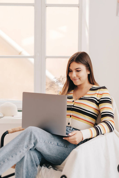 Attractive young caucasian woman use laptop computer, sitting on armchair in bright living room. Distance work concept - Φωτογραφία, εικόνα