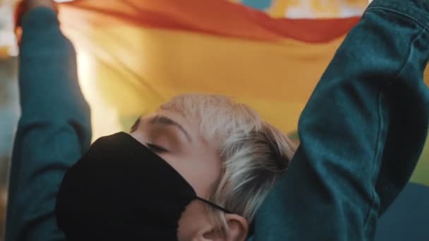 Mulher loira jovem orgulhoso com máscara facial acenando bandeira do arco-íris. Fechar - Filmagem, Vídeo