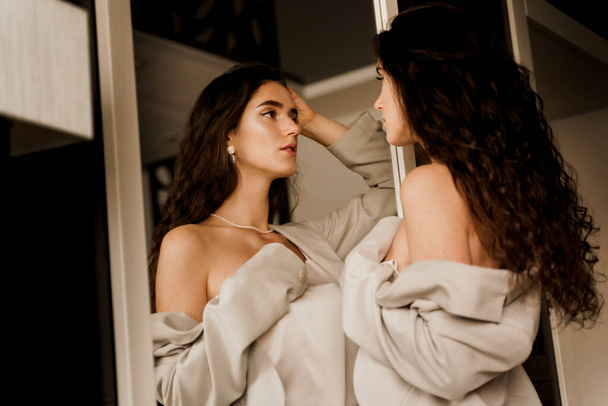 Mode, elegantes und sexy professionelles Model, das in der Nähe eines Spiegels posiert und ihr Spiegelbild betrachtet. Wunderschöne junge Frau im klassischen Anzug im Fotostudio. - Foto, Bild