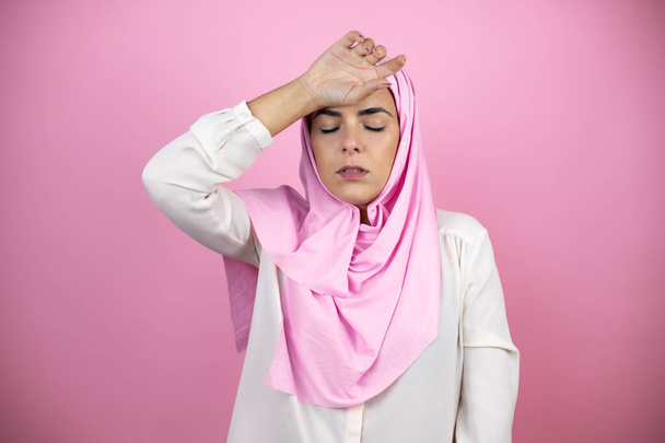 Joven mujer árabe hermosa con hiyab islámico sobre fondo rosa aislado tocando la frente para la enfermedad y la fiebre, gripe y resfriado, el virus enfermo - Foto, imagen