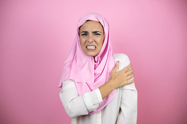 Junge schöne arabische Frau trägt islamischen Hijab über isoliertem rosa Hintergrund mit Schmerzen an der Schulter und einem schmerzhaften Ausdruck - Foto, Bild