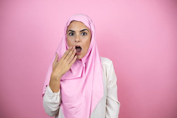 Young beautiful arab woman wearing islamic hijab over isolated pink background surprised covering her mouth - Fotoğraf, Görsel