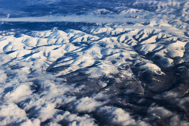 Snowy mountains from a bird's eye view on a clear blue sky with clouds. - Foto, Imagem