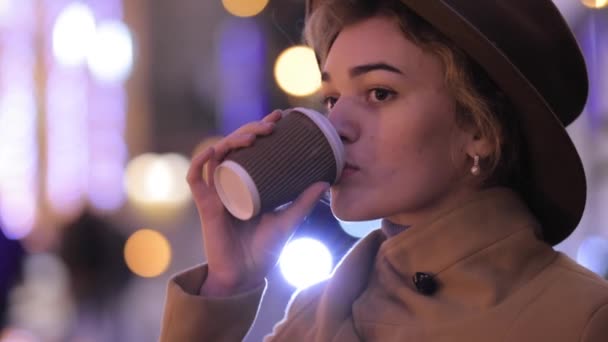 Kaunis nainen hattu ja takki juo kahvia yöllä kaupunki - Materiaali, video