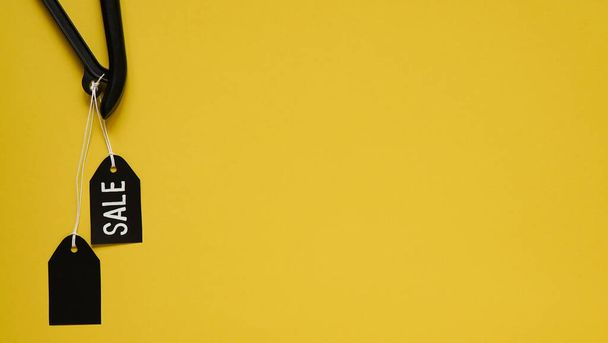 Cintre à vêtements noir avec étiquettes noires vierges sur fond jaune, vue de dessus, pose plate, espace de copie, gros plan - Photo, image