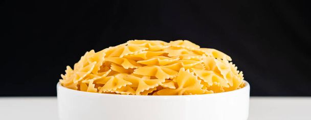 Nyers száraz, főzés nélküli Farfalle tészta spagetti tészta fehér tál fa háttér bazsalikom paradicsom pesto mártással Házi készítésű olasz élelmiszer bio teljes kiőrlésű vegán spagetti egészséges étel - Fotó, kép