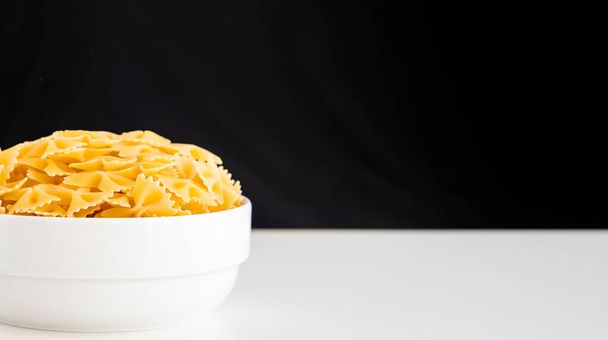 Roh getrocknete, ungekochte Farfalle Nudeln Spaghetti Nudeln auf weißem Schüssel hölzernen Hintergrund für Basilikum Tomaten-Pesto-Sauce Hausgemachte italienische Lebensmittel Bio-Vollkorn-vegane Spaghetti für eine gesunde Mahlzeit - Foto, Bild