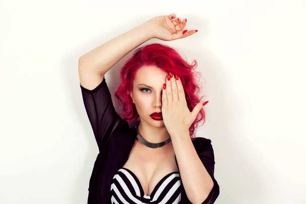Mujer modelo de moda chica mostrando maquillaje, labios rojos en conjunto con las uñas manicura combinado con el pelo y la ceja, cubriendo el ojo con las manos mirando a la cámara sobre fondo blanco beige - Foto, Imagen