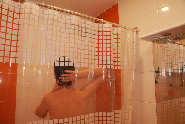 La chica toma una ducha del cabezal de la ducha fijado en el soporte en el baño. - Foto, imagen