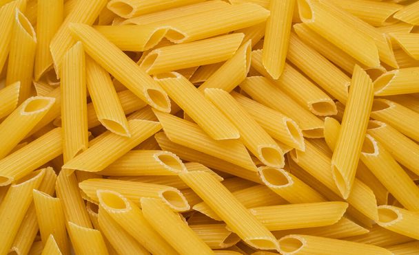 Syrové suché nevařené těstoviny penne v misce na bílém pozadí. Dobrý pro bazalka rajčatová pesto omáčka Domácí čerstvé italské jídlo styl bio celozrnné pšeničné veganské špagety nudle pro zdravé jídlo - Fotografie, Obrázek