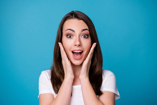 Closeup photo of attractive pretty funny lady good mood charming cute straight hairstyle arms on cheeks shocked amazing news wear casual white t-shirt isolated blue color background - Foto, afbeelding
