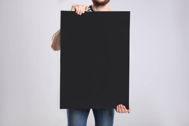 Man holding blank poster on light grey background, closeup - Foto, Bild