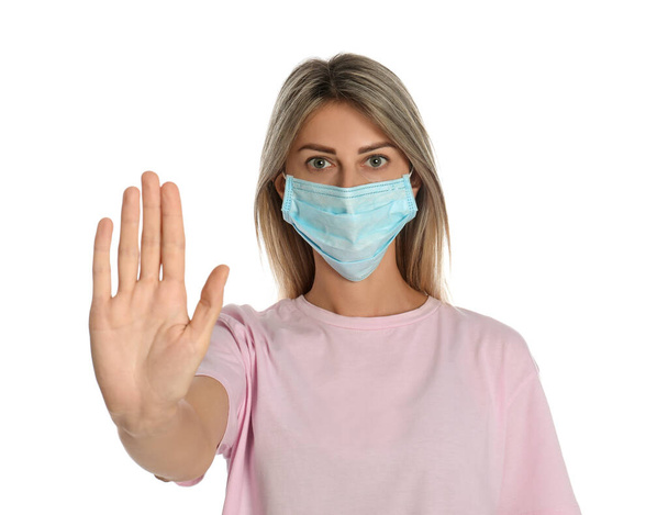 Woman in protective mask showing stop gesture on white background. Prevent spreading of coronavirus - Photo, image