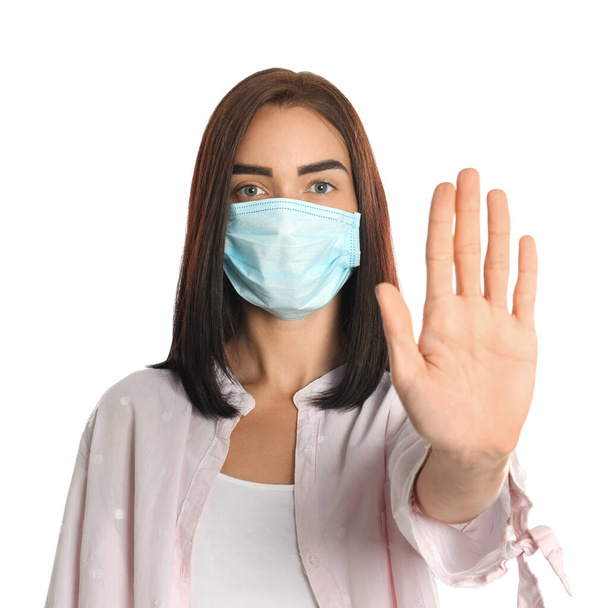 Young woman in protective mask showing stop gesture on white background. Prevent spreading of coronavirus - Photo, Image