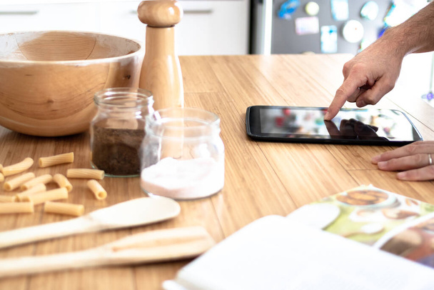 mies valmistelee ruokaa keittiössä käsittelyssä Webistä tabletilla online-ruoanlaitto resepti, jossa hänen sormensa tabletin, keittokirja puinen keittiö pöytä. moderni nainen ruoanlaitto - vain kädet - Valokuva, kuva