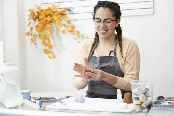 Hispanische Frau lächelt während ihrer Arbeit in ihrer Konditorei - junge Frau arbeitet mit Fondant an der Dekoration einer Torte - junge lateinamerikanische Unternehmerin Konditorin - Foto, Bild