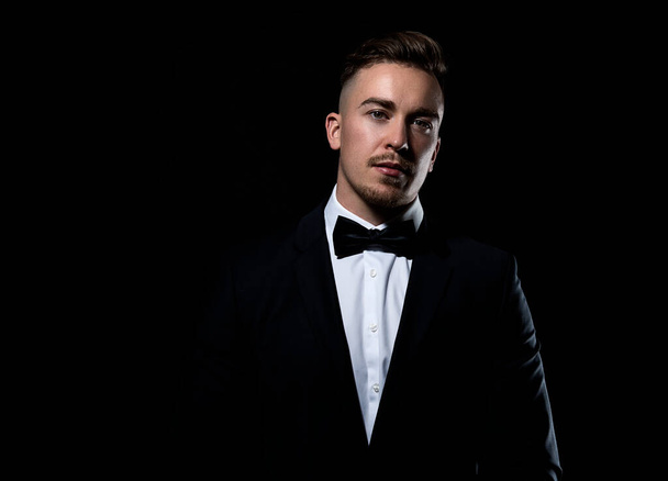 Handsome young man wearing black tux with bow tie and posing on black background - Zdjęcie, obraz