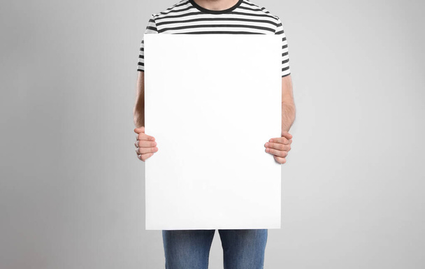 Man holding blank poster on light grey background, closeup - Foto, afbeelding