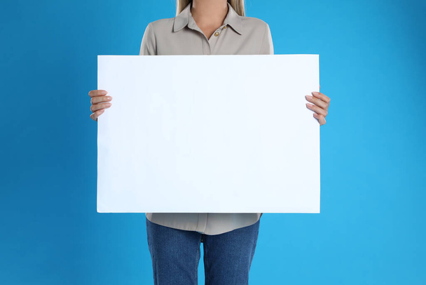 Woman holding blank poster on blue background, closeup - Фото, изображение