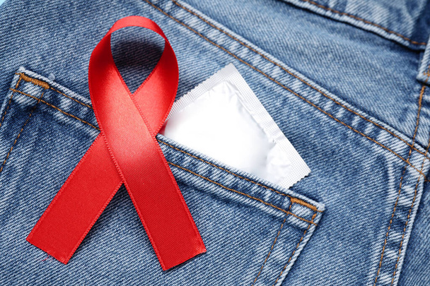 Jeans with red ribbon and condom, closeup. AIDS disease awareness - Foto, afbeelding
