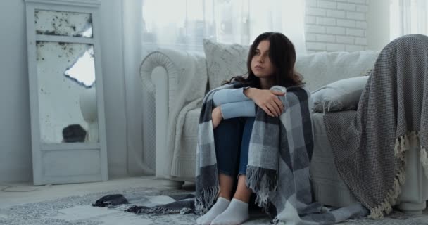 Traurige depressive junge Frau, die allein auf dem Boden sitzt, in Plaid gehüllt, Schmerz empfindet und zu Hause unter Einsamkeit leidet - Filmmaterial, Video
