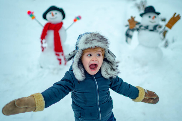 Winter portrait of little boy child in snow Garden make snowman. Child playing with Snowman on snow background. Winter children in frosty winter Park. - Фото, изображение