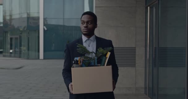 Depresso afro-americano lavoratore ufficio maschile lasciando business center edificio con scatola di roba personale - Filmati, video