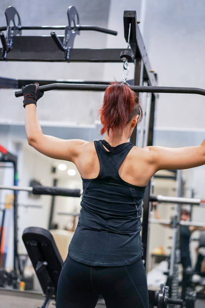 Fille entraînement athlétique pompage vers le haut des muscles du dos tirer vers le bas dans la salle de gym. - Photo, image