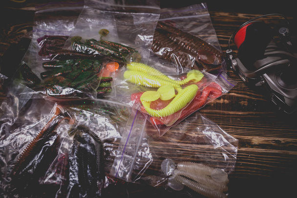 Spinning rod with a reel and silicone baits in plastic bags. Studio photo on a wooden background. Flat lay - Photo, Image