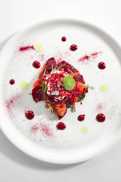 Baked beet salad with citrus fruits and stracciatella on restaurant plate isolated. Red salat with sliced beets, grapefruit, pomegranate, cheese ice cream topview - Zdjęcie, obraz