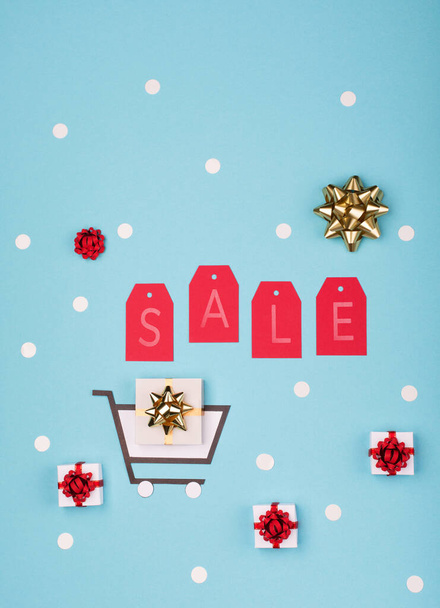 Super Sale day or Singles day concept. Shopping trolley, gift boxes and red tags on blue paper background. Online shopping of China. Top view, flat lay, copy space. - Photo, Image