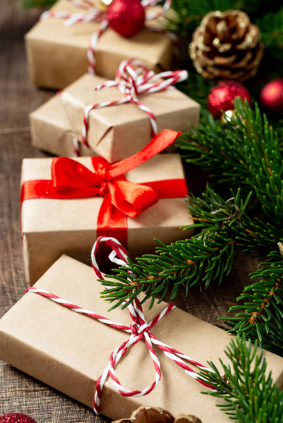Geschenkdozen in ambachtelijk papier. Kerst achtergrond. Kerstgeschenken onder sparren takken op een bruine houten ondergrond - Foto, afbeelding